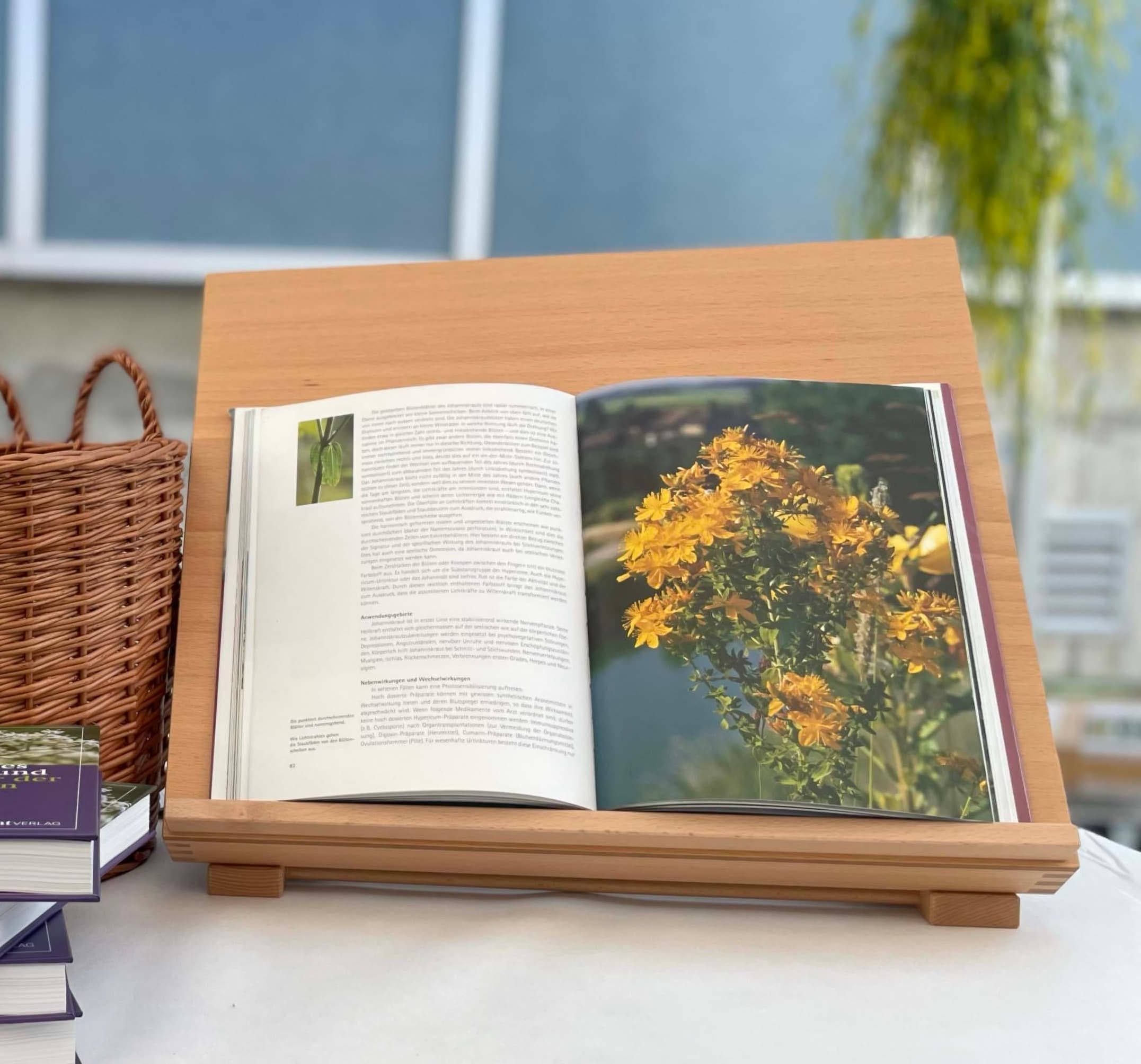 Un livre ouvert sur un support en bois présente une page de texte à gauche et une photo de fleurs jaunes à droite, avec un panier tressé à côté sur une table.
