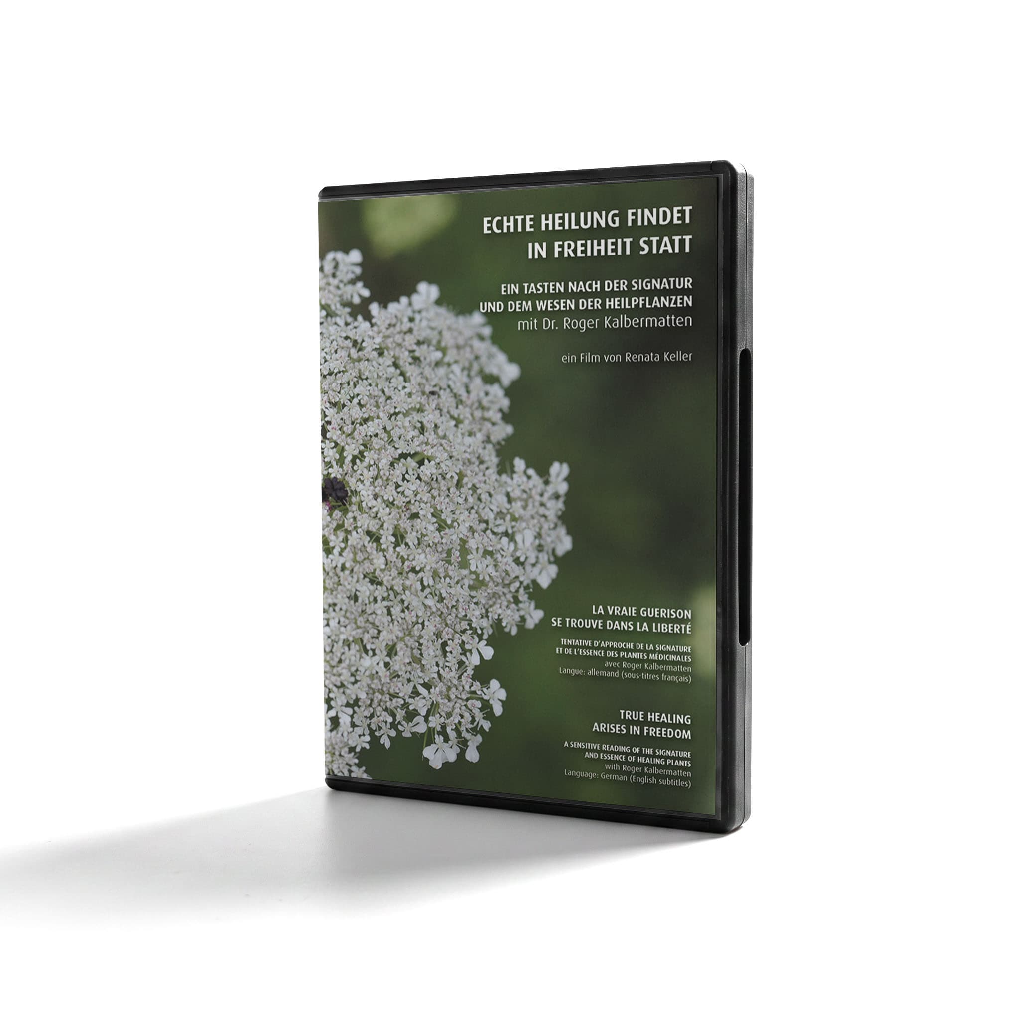 DVD-Hülle mit dem Titel 'Echte Heilung findet in Freiheit statt' zeigt ein Nahaufnahmebild von weißen Blüten eines Heilpflanzenmotivs vor grünem Hintergrund. Text ist auf Deutsch, Französisch und Englisch vorhanden.