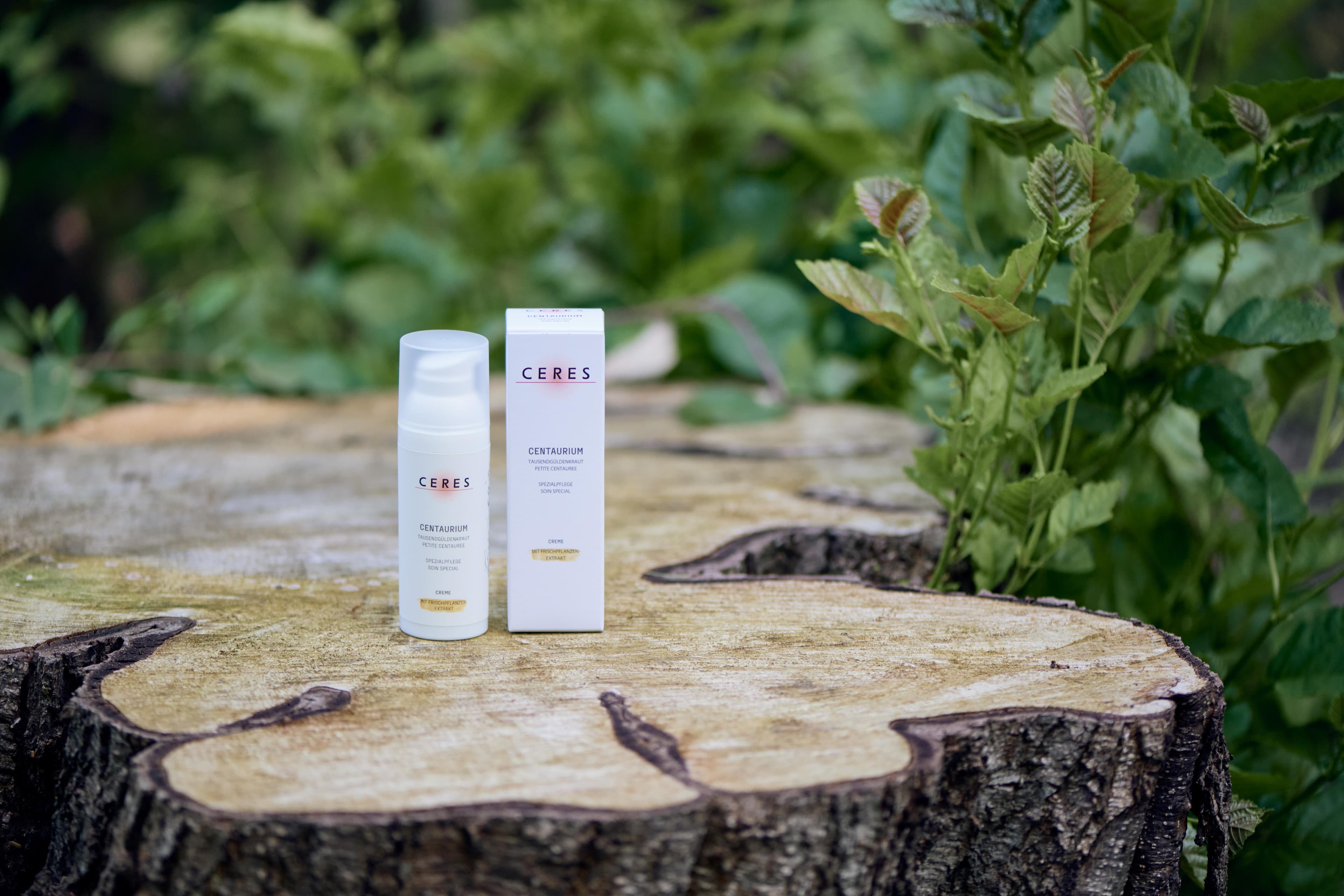 Eine Flasche und eine Verpackung des CERES Centaurium Naturkosmetikprodukts stehen auf einem Baumstumpf im Freien, umgeben von grünen Pflanzen.